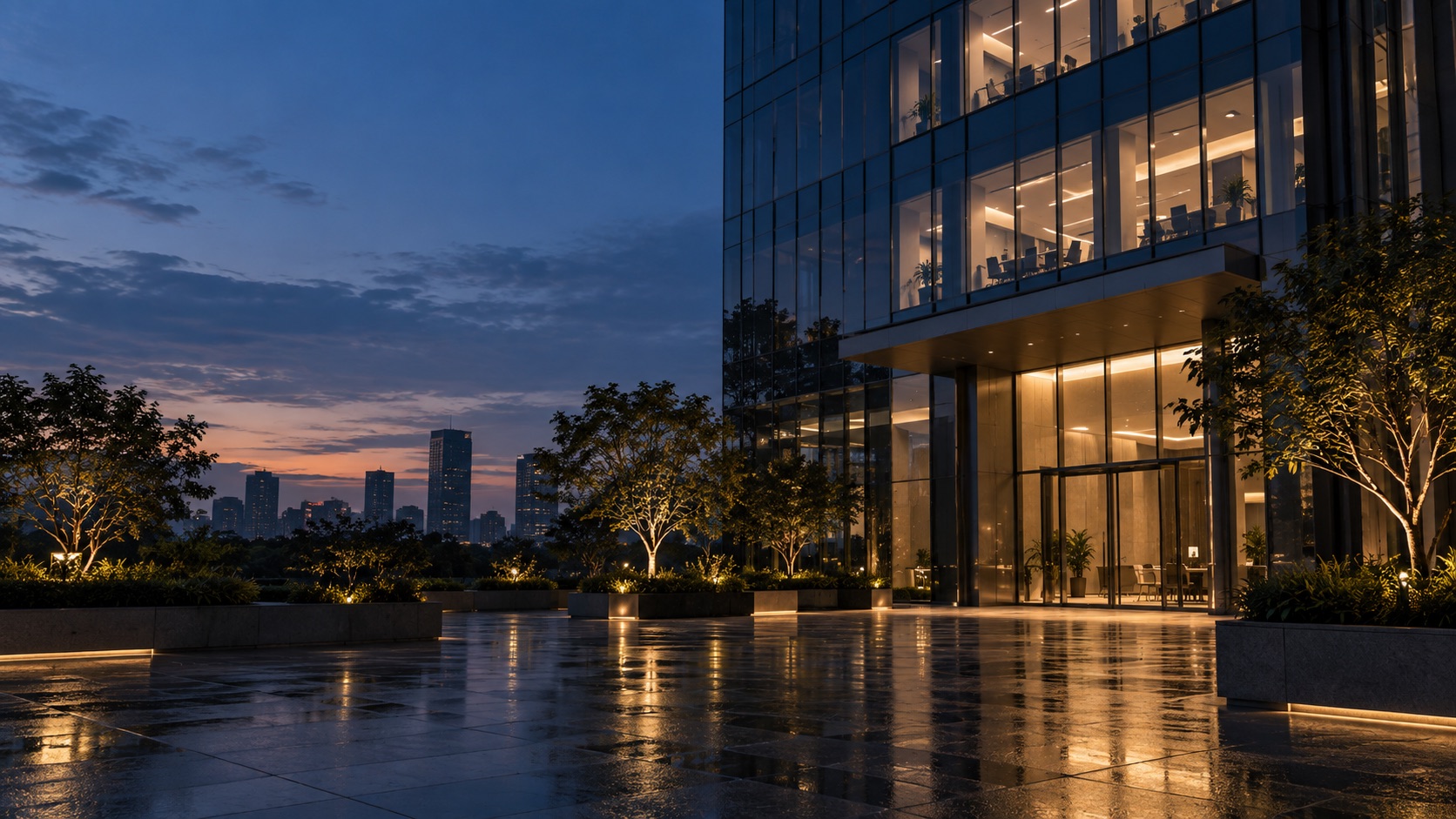 A glass office tower at dusk, interior lights on across the floors above a wet plaza